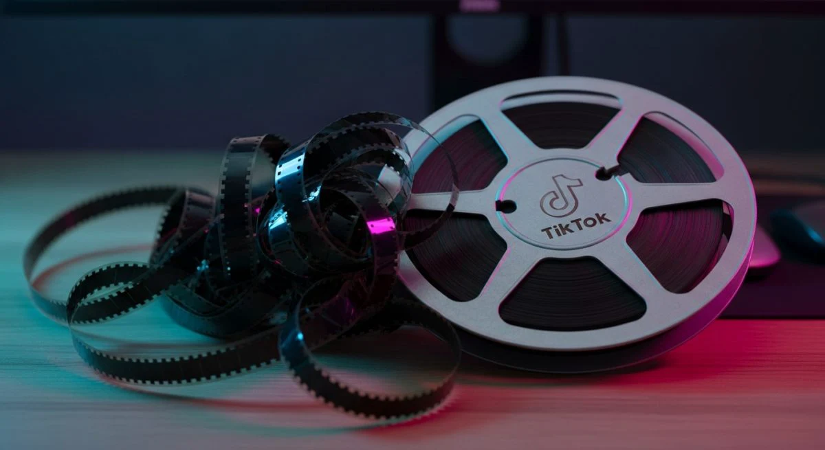 Carrete 16mm enredado sobre escritorio con luz cian y magenta y logo de TikTok