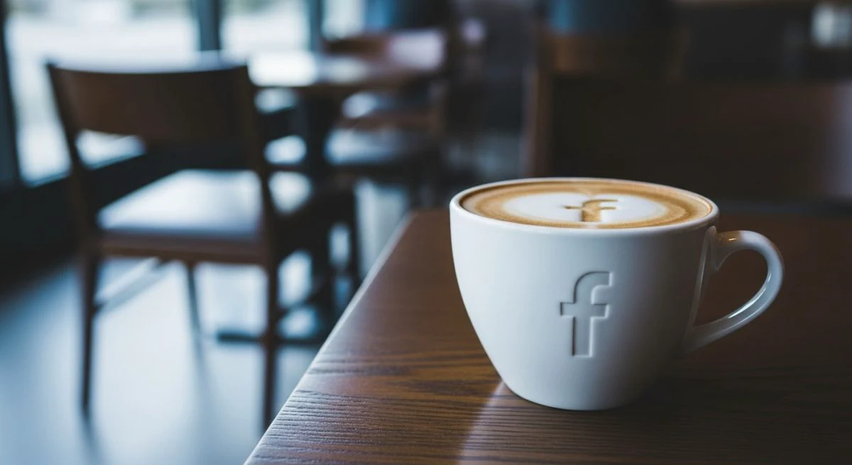 Taza café blanca con logo Facebook sobre mesa madera oscura