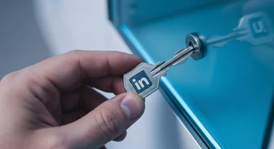 Mano sosteniendo llave metálica grabada LinkedIn frente gabinete vidrio azul