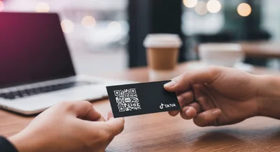 Manos intercambian tarjeta negra con código QR y logo TikTok